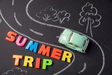 Toy car on the road and inscription plastic letters summer trip on chalkboard