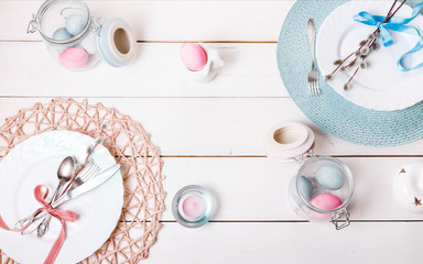 Easter table setting with pink and blue eggs and cutlery. Holidays background. Festive white wooden table