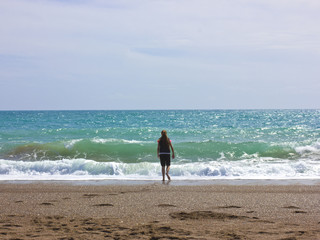 A young girl stands on the beach near the blue sea