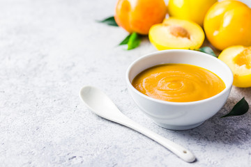 Peach and yellow plum sauce in ceramic bowl and fresh golden plums on concrete background. Selective focus, space for text. 