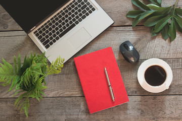 Open laptop with red notebook on office wooden desk table. Top view.