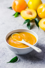 Yellow plum puree in ceramic bowl  and fresh golden plums on concrete background. Selective focus, space for text. 