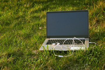 laptop with headphones stands on green grass