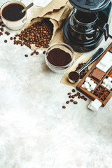 Variety things for prepare coffee. Roasted beans, ground coffee, scoop, electric coffee machine and assortment of sweets and spices to eat with on light background. Top view copyspace