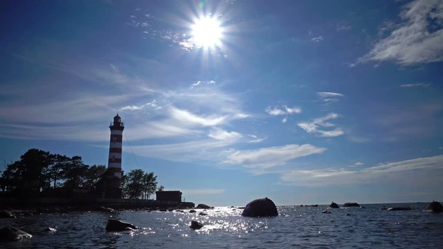 The building of the old beacon on the seashore against the background of the sky with brightly consecrating sun.Sunshine over a Lighthouse. St. Petersburg. Gulf of Finland