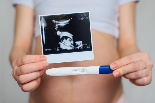 ultrasound picture and positive pregnancy test in the hands of a pregnant girl on the background of the abdomen