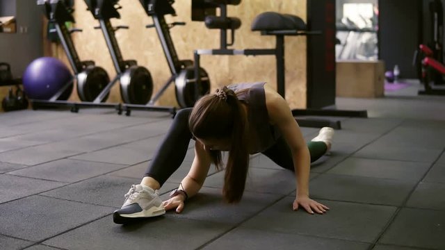 Attractive brunette female in her 20's stretching out in the gym, preparing leg muscles to do the splits.