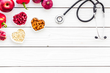 Products good for heart and blood vessels. Vegetables, fruits, nuts in heart shaped bowl near stethoscope on white wooden background top view copy space