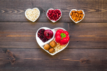 Food which help heart stay healthy. Vegetables, fruits, nuts in heart shaped bowl on dark wooden background top view