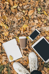 Flat lay view of autumn leaves, tablet, phone and paper cup of coffe. From above with legs