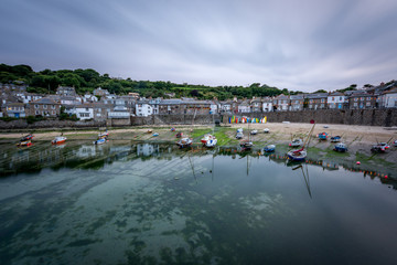Fototapeta na wymiar Calm clear water with boats on beach at the picturesque fishing village of Mousehole in Cornwall