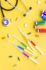 Fototapeta na wymiar Medical examination and treatment concept. Stethoscope, syringe, pills on yellow background top view