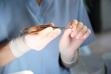 Hands of a dental surgeon in protective gloves with a tool for treating a patient