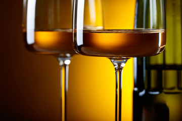 Glasses and bottle of white wine on a yellow background.