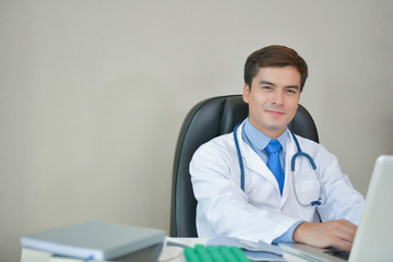 Smiling doctor posing in the office, he is wearing a stethoscope, medical staff on the hospital background