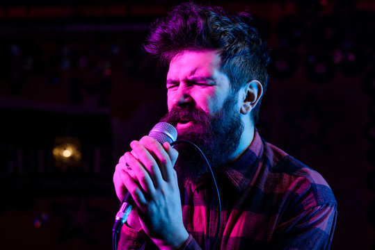 Man with enthusiastic face holds microphone, singing song, black background.