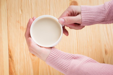 female hands holding coffee with milk on a wooden background