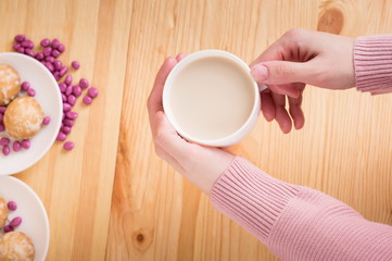 female hands holding coffee with milk on a wooden background