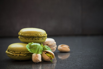 Sweet green pistachio flavor macaroons with nuts and leaves on dark stone background. Close up, selective focus