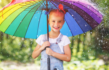 Happy child girl laughs and plays under summer rain with an umbrella.