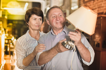 Mature couple is shopping the old lamp in the antique store.