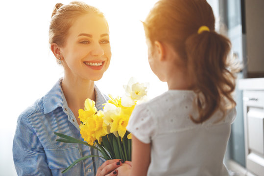 happy mother's day! child daughter   gives mother a bouquet of flowers to narcissus and gift
