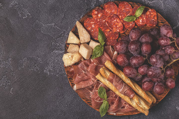 Prosciutto, sausage, wine, grape, parmesan on dark table.