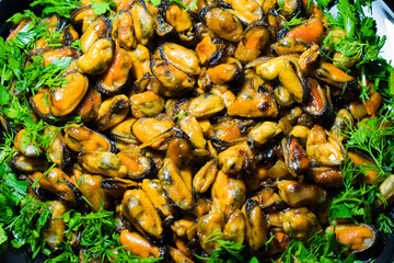 Coffee fried appetizing mussels on a dish, decorated with greenery.