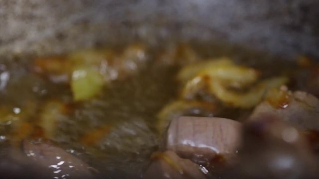 Cook stirring meat and onions with slotted spoon when frying them in oil in cast iron skillet, close up shot