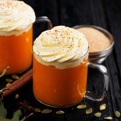 Pumpkin smoothie, spice latte with whipped cream on top on dark  wooden background.