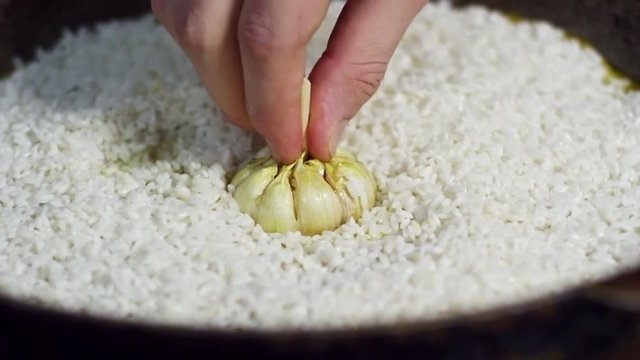 Close up shot of frying pan with white rice in it, cook putting head of garlic in the center when cooking pilaf
