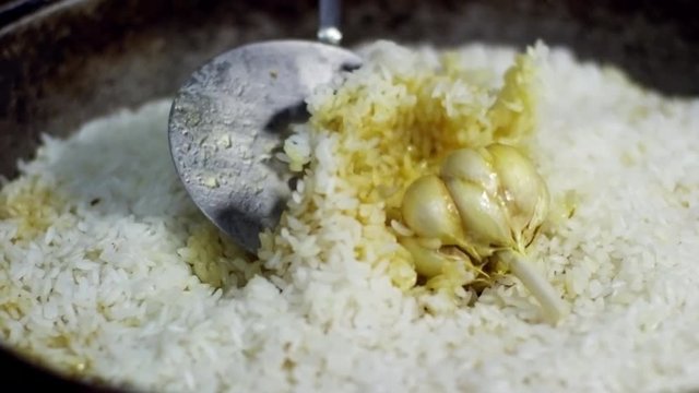 Cook stirring pilaf with slotted spoon, close up shot of dish with head of garlic in the center