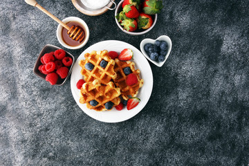 Traditional belgian waffles with fresh fruit and powder sugar on wooden board