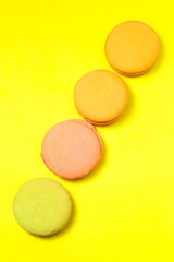 Delicious four multicolored macaroon on a yellow background