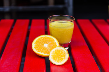 Yellow smoothie on the red table with slices of orange and lemon