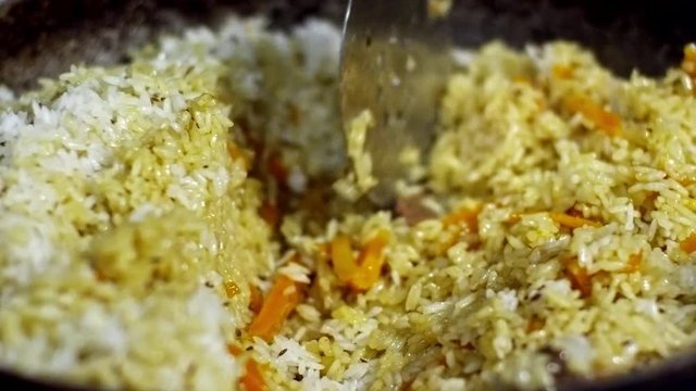 Close up shot of rice pilaf with meat and carrots seasoned with cumin seeds, cook stirring it with slotted spoon