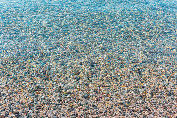Background of blurred bright colorful sea stones under water. Iridescent sunlight on the stones. Transparent clear water of sea. Toned photo