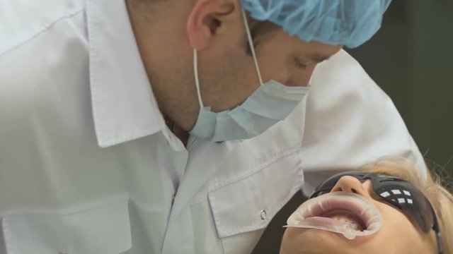 Dentist is treating a patient in a modern dental office. Orthodontist works with an assistant. The operation is carried out using a cofferdam. The client is inserted and restored teeth, make a denture