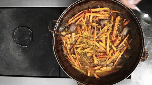 Close up shot of cook adding ground coriander or turmeric to red meat and carrots when cooking pilaf, top view