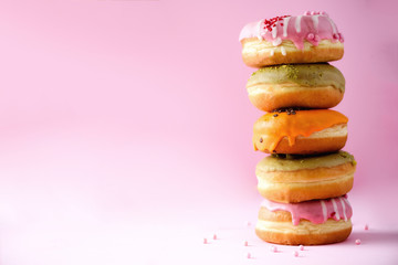 Stack of glazed colorful assorted donuts with sprinkles on pink background. Copy space. Sweet doughnuts for kids - obrazy, fototapety, plakaty