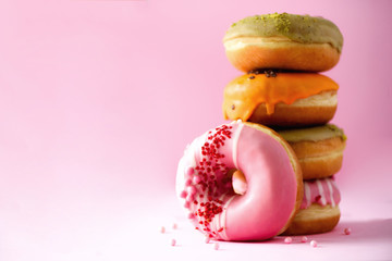 Stack of glazed colorful assorted donuts with sprinkles on pink background. Copy space. Sweet doughnuts for kids
