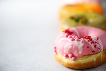 Stack of glazed colorful assorted donuts with sprinkles on grey cement background. Copy space. Sweet doughnuts for kids