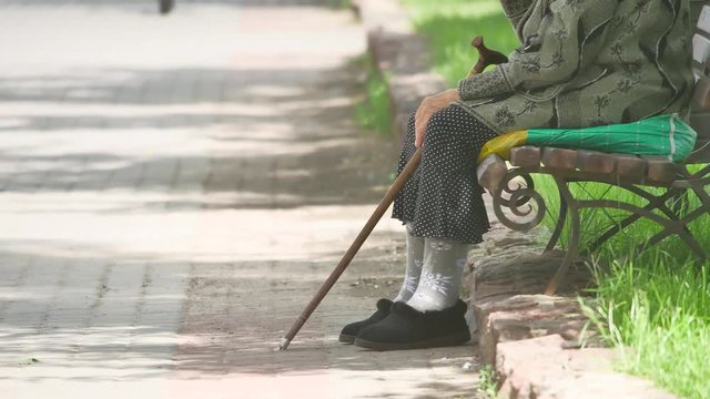 grandmother pensioner homeless poor disabled with crutch sitting on a bench in a park Russia concept poverty lifestyle outdoors