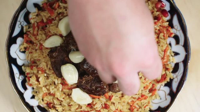 Close up shot of rotating plate of beef pilaf with carrot and cloves of garlic on top, chef sprinkling it with pomegranate seeds, above view
