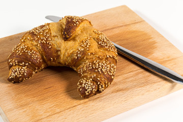 Sesamcroissant neben einem Küchenmesser auf einem Holzbrettchen
