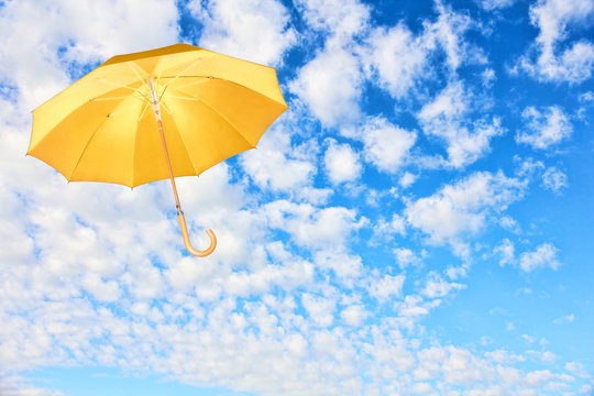 Yellow umbrella flies in sky against of white clouds.Wind of change concept.Mary Poppins Umbrella.