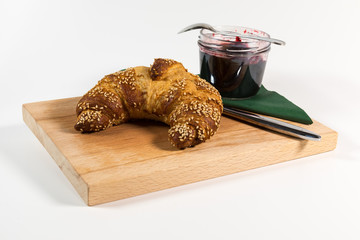 Sesame croissant and jam on a wooden plate