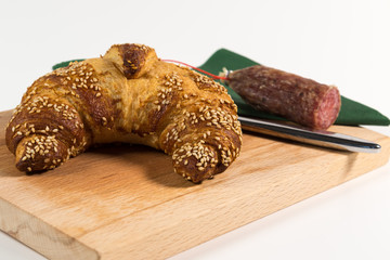 Sesame croissant and a salami on a wooden plate for a little breakfast