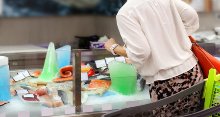 Woman shopping for fresh fish seafood in supermarket retail store 