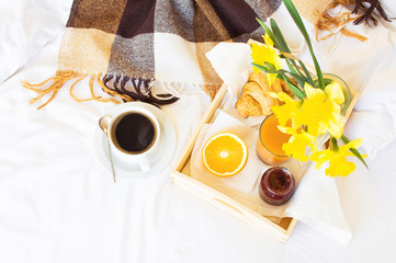 Morning breakfast in bed wooden tray with a cup of coffee croissant orange juice fresh orange jam bouquet of flowers daffodils. Top view Morning at Hotel Background Concept Interior Copy Space